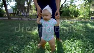 小宝宝学会走路.. 第一步。 父母在教孩子在草地上迈出第一步